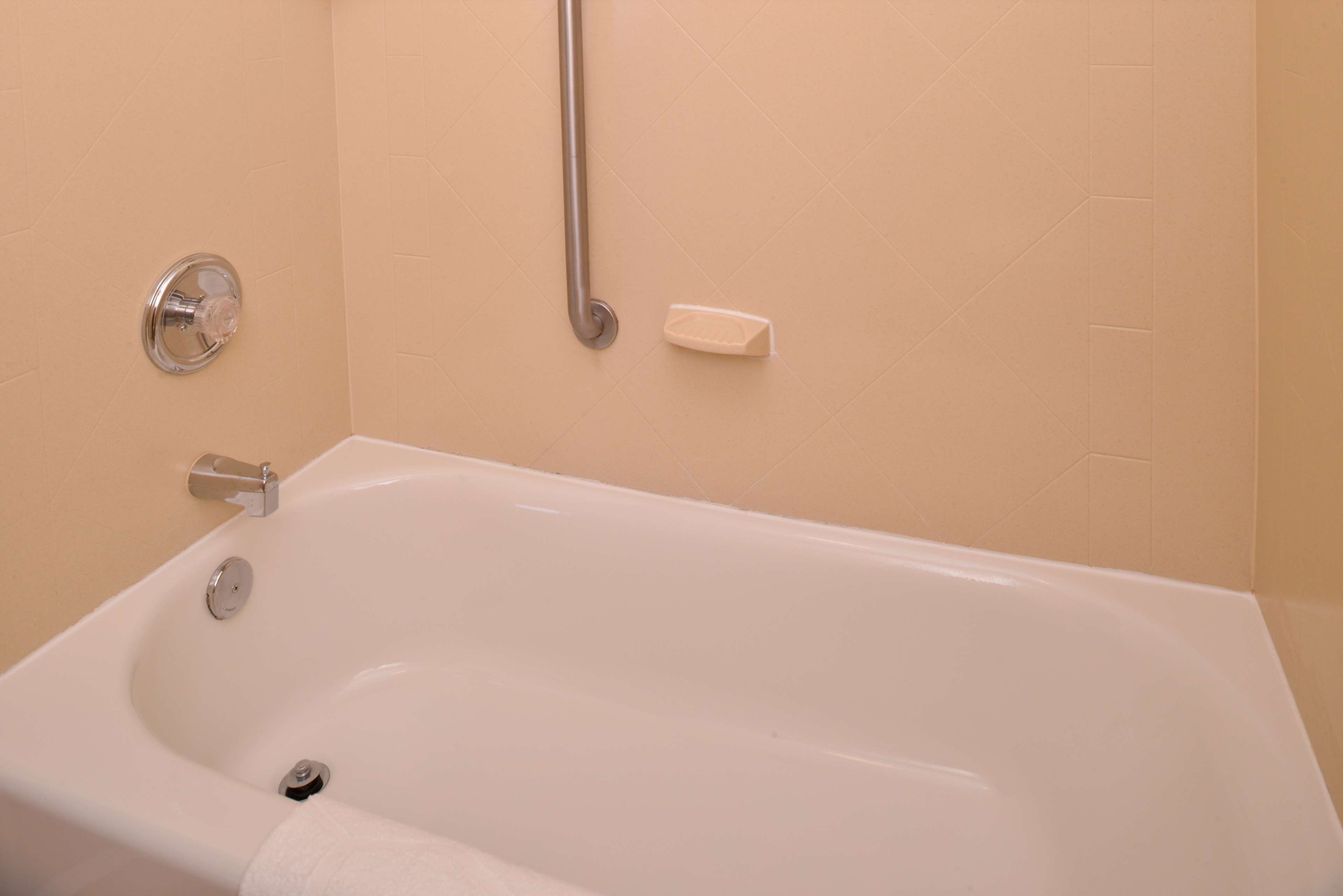 Una bañera estándar con grifo, cabezal de ducha manual y un perchero para toallas.