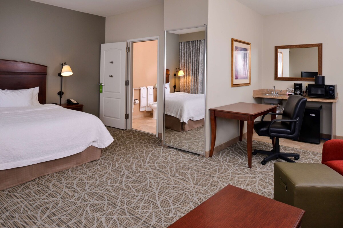 A hotel room with a bed, a desk, a chair, a microwave, a coffee maker, and a mirror.