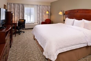 Una habitación de hotel con una cama grande, un escritorio con televisor, una silla y una ventana con cortinas.