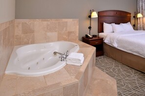 Habitación de hotel con una bañera grande, una mesita de noche con teléfono y una cama bien hecha.