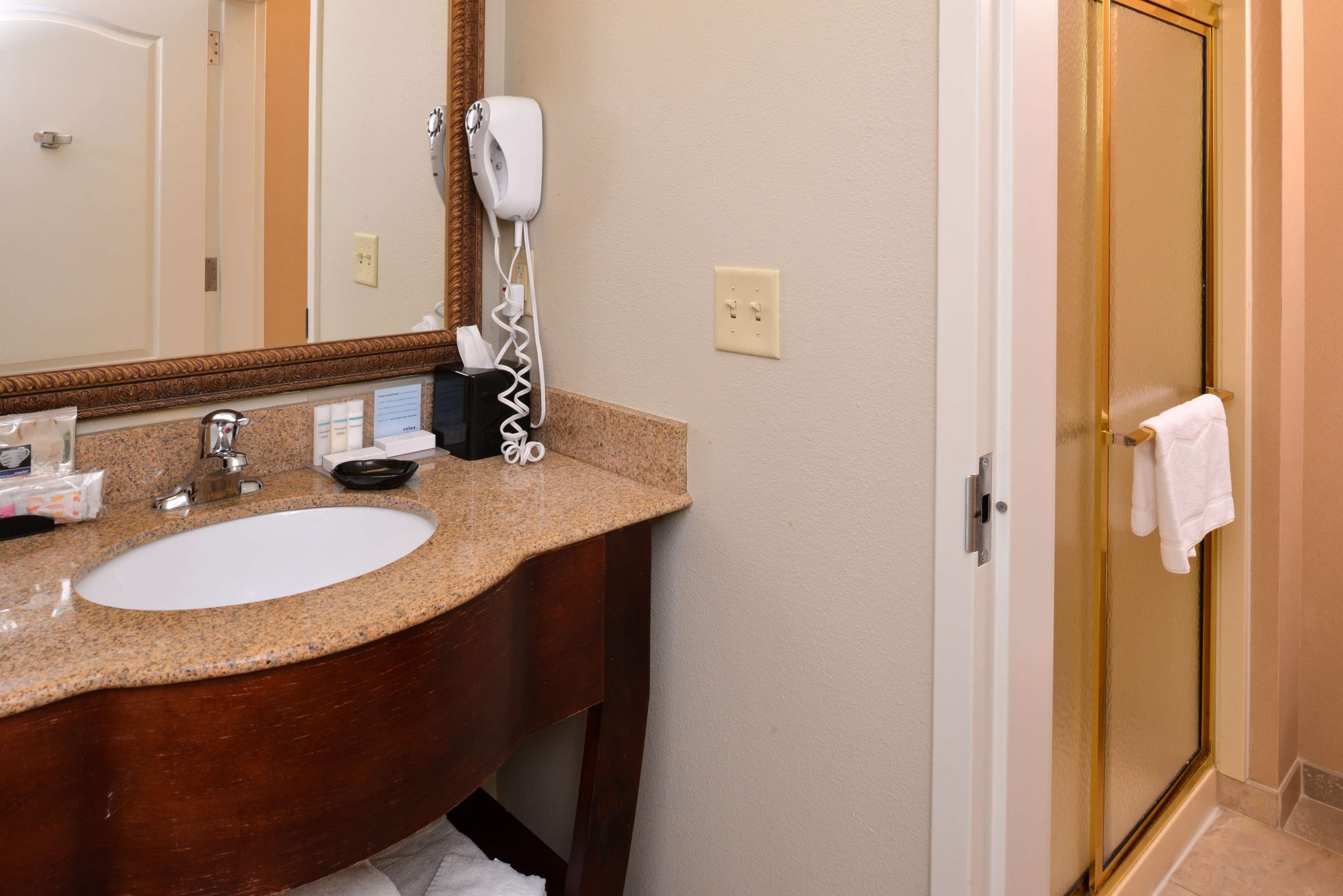 A hotel bathroom with a granite countertop sink, a hairdryer, and a towel rack.