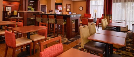 A hotel dining area with multiple tables and chairs, a reception desk, and a clock on the wall.