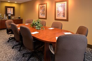 Un salón de conferencias con una mesa de madera, seis sillas, una planta en maceta y obras de arte enmarcadas en las paredes.