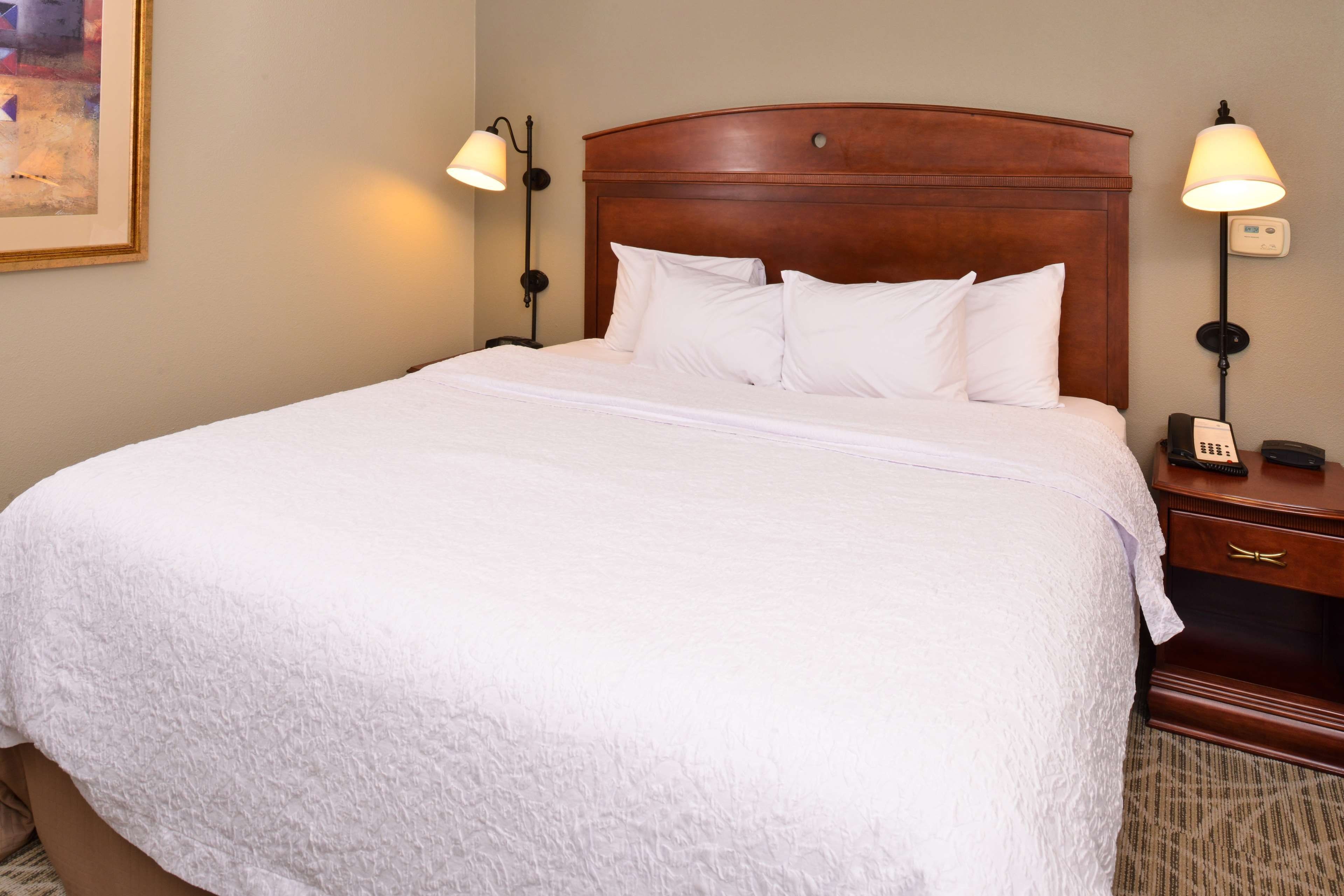 A hotel room with a large bed, two bedside tables, a nightstand, and a lamp.