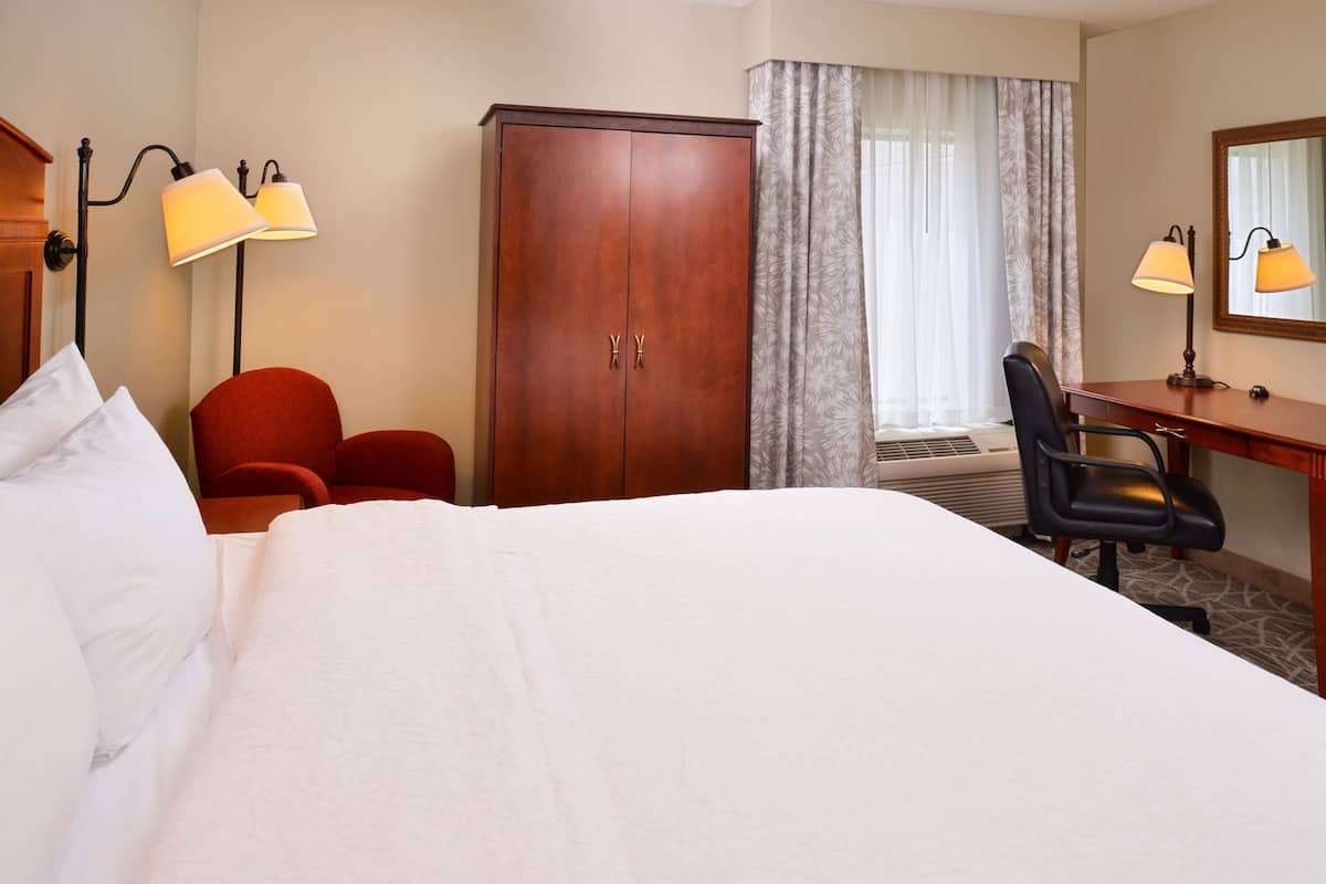 A hotel room with a large bed, a desk with a chair, a wardrobe, and two wall-mounted lamps.