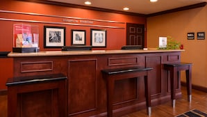 A reception desk with a wooden finish, framed pictures on the wall, and a welcome sign. - Hampton Inn by Hilton Litchfield (Litchfield)