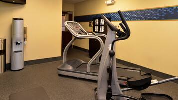 Un gimnasio con cinta de correr y elíptica, dispensador de agua y basurero.