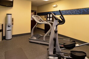 Un gimnasio con cinta de correr y elíptica, dispensador de agua y basurero.