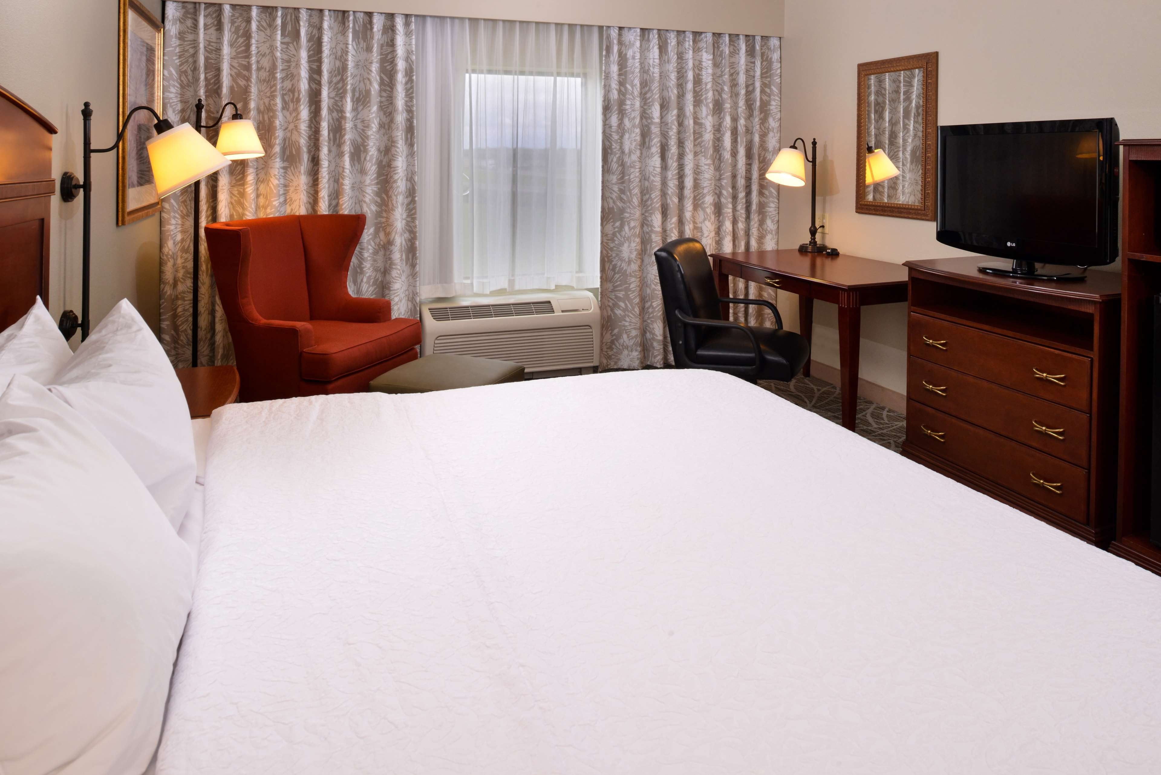 Ein Hotelzimmer mit einem Bett, einem Schreibtisch, einem Sessel, einem Fernseher und zwei Lampen.