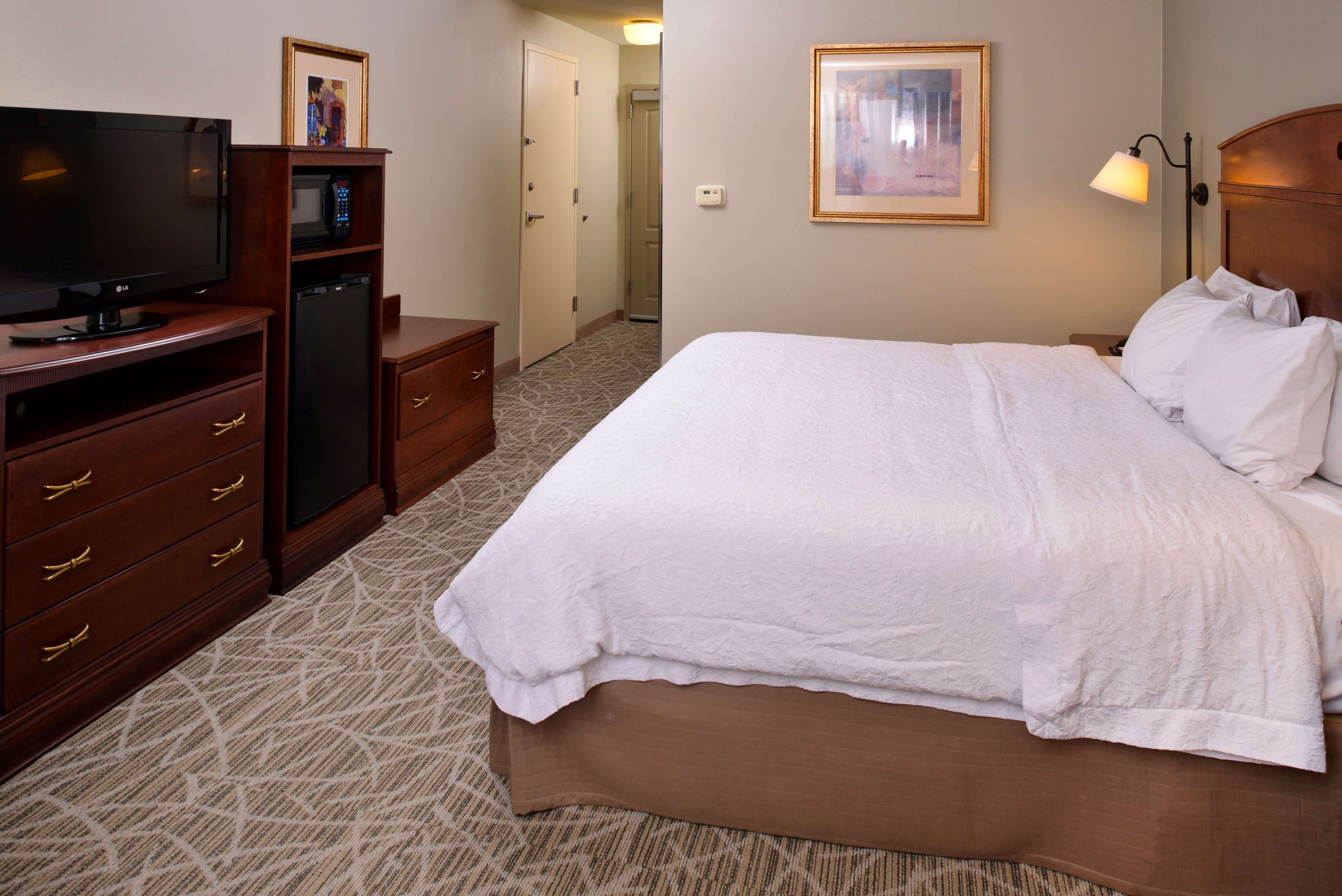 Een hotelkamer met een bed, een televisie, een minibar, een bureau en een deur naar een andere kamer.