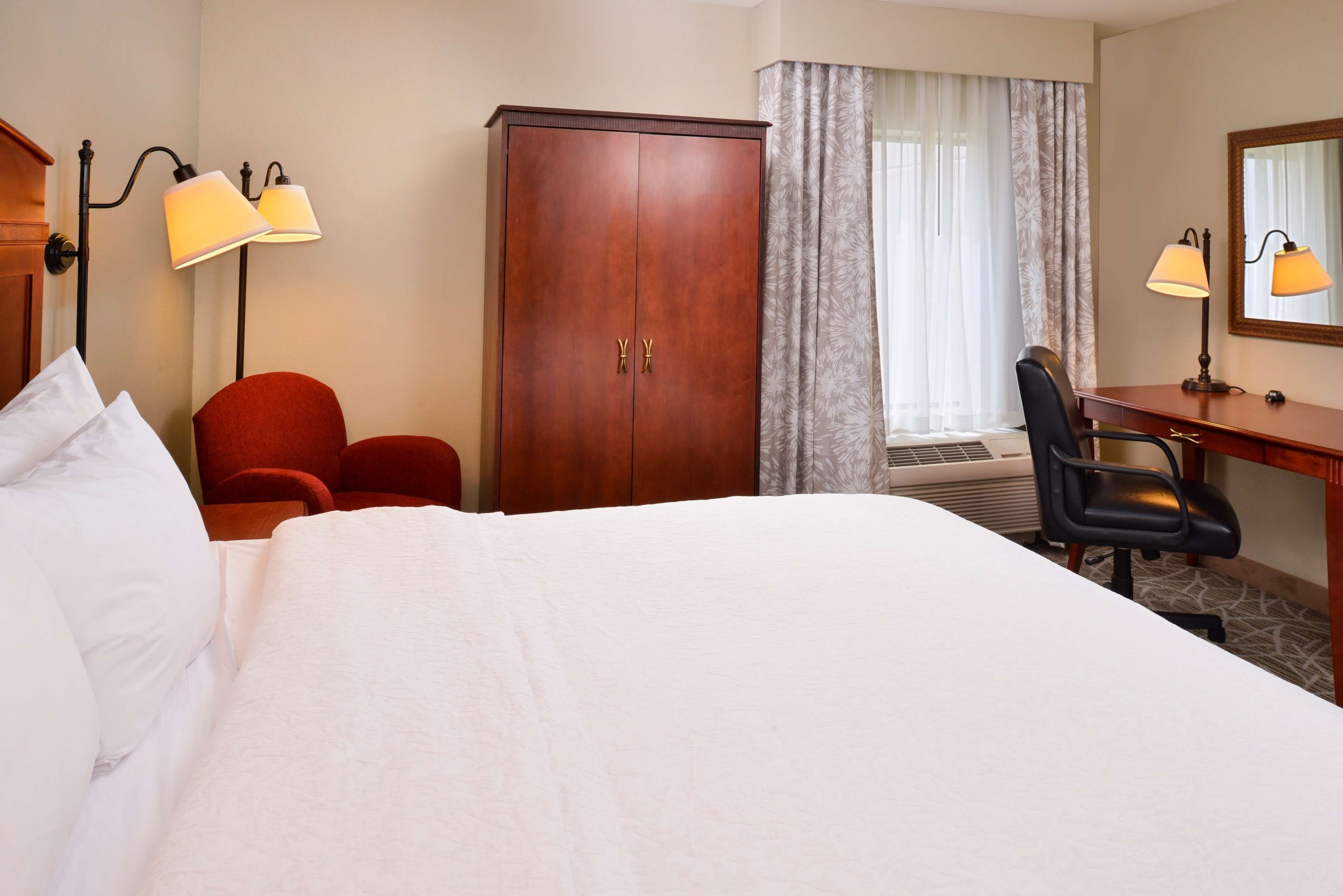 Une chambre d’hôtel comprenant un lit, un bureau, une chaise, une armoire et deux lampes.