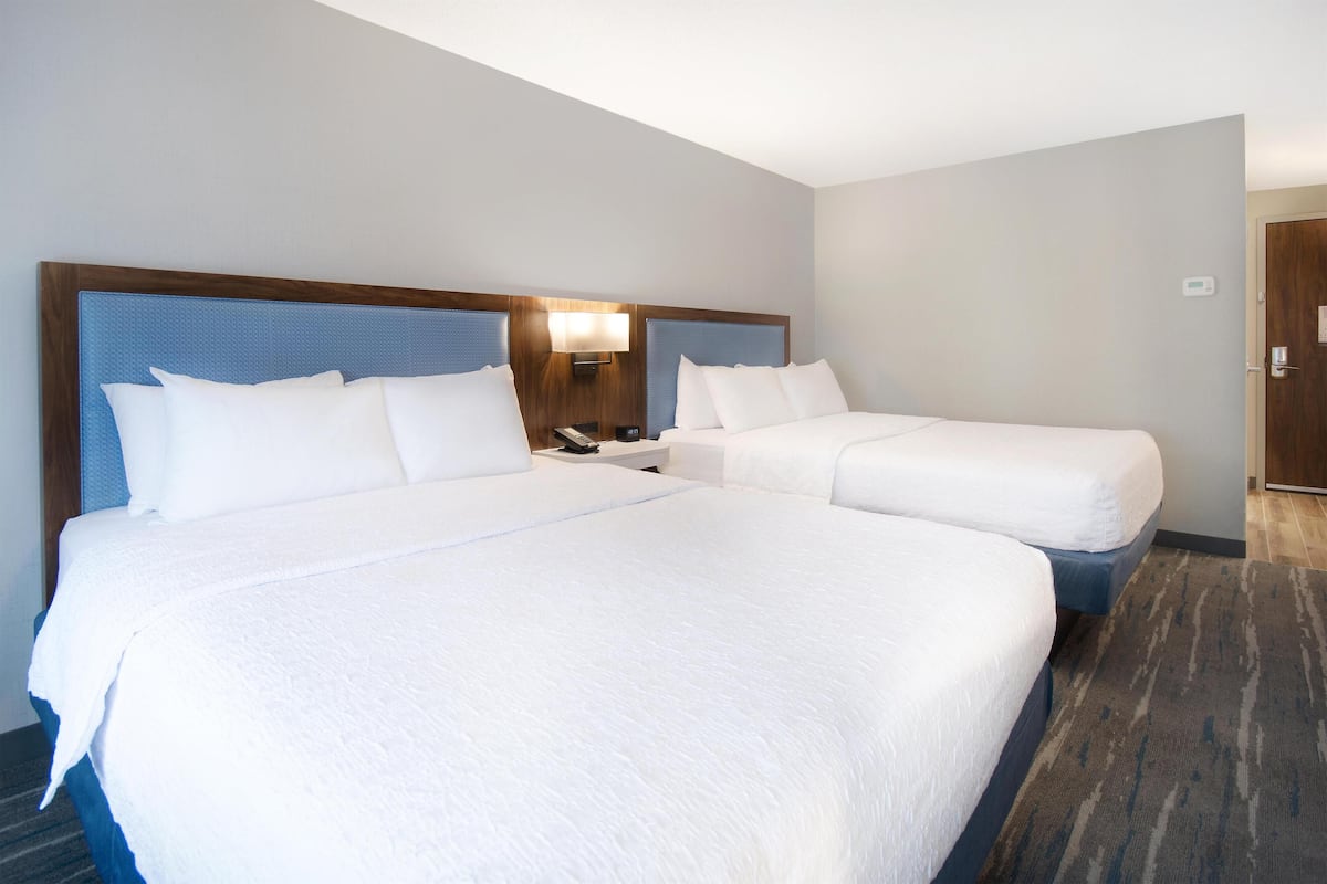 Una habitación de hotel con dos camas, una mesita de noche con lámpara y una puerta.