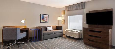 Una habitación de hotel con escritorio, sofá, televisor y cómoda.