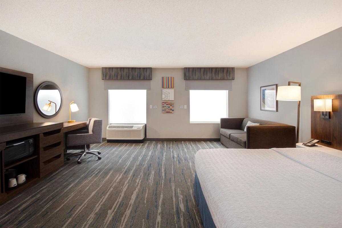 Una habitación de hotel con una cama grande, un escritorio con computadora, una silla, un televisor y una ventana.