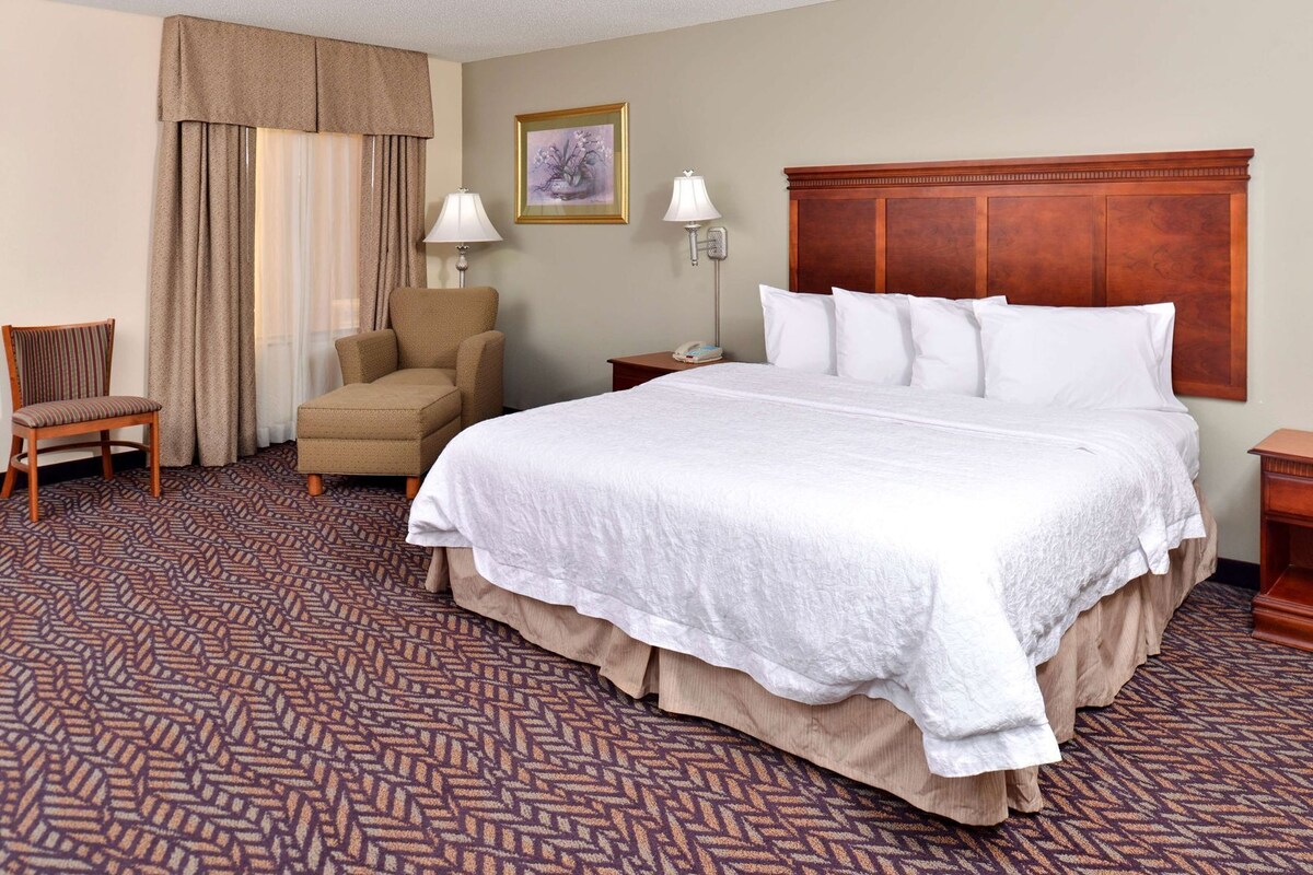 A hotel room with a large bed, a chair, a desk, and a lamp.