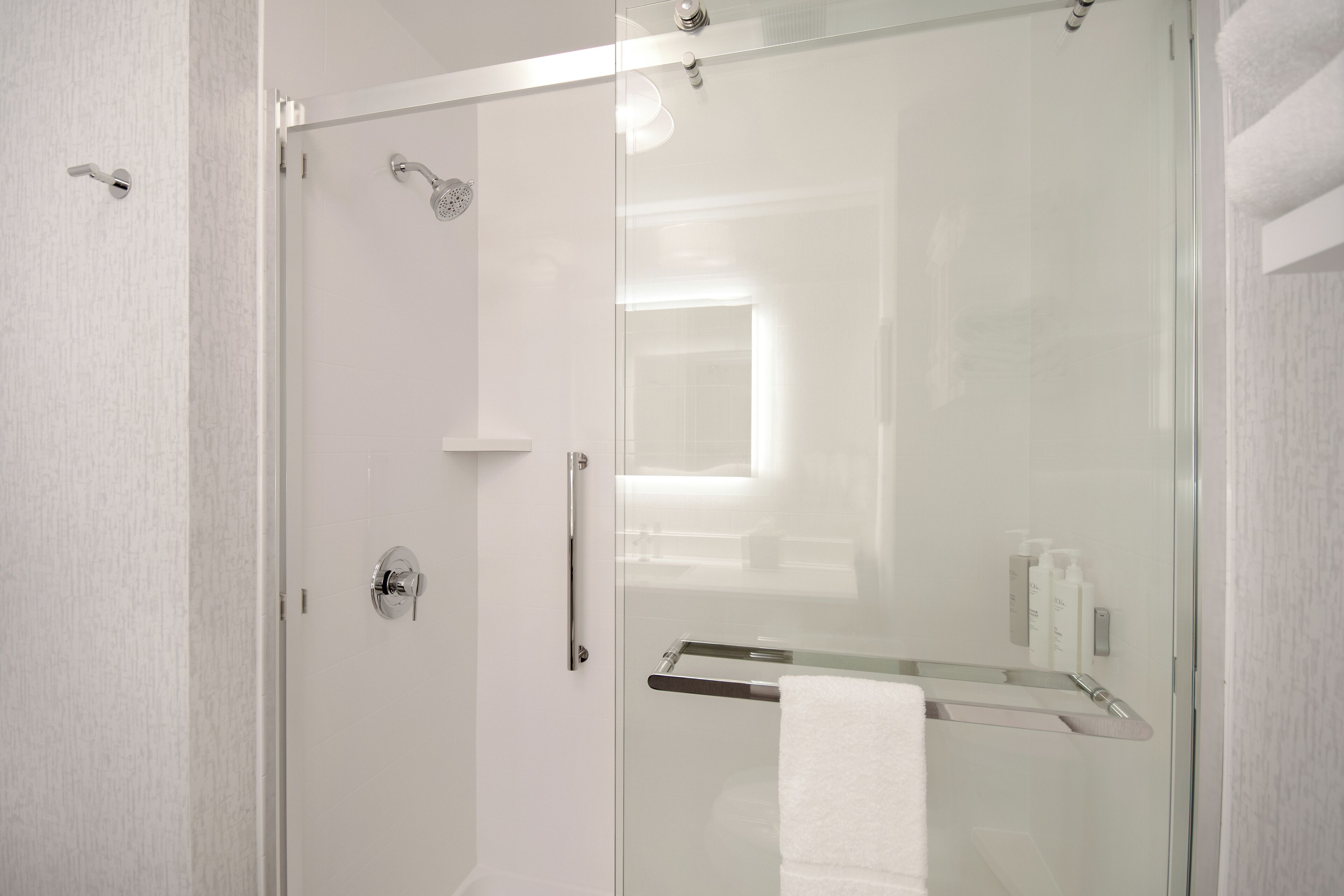 A modern bathroom with a glass shower enclosure, a white towel rack, and a visible bottle of shampoo.
