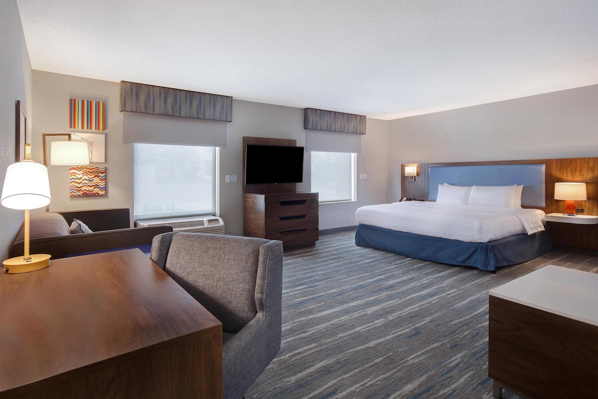 Habitación de hotel con cama, escritorio, silla, televisor y cómoda.