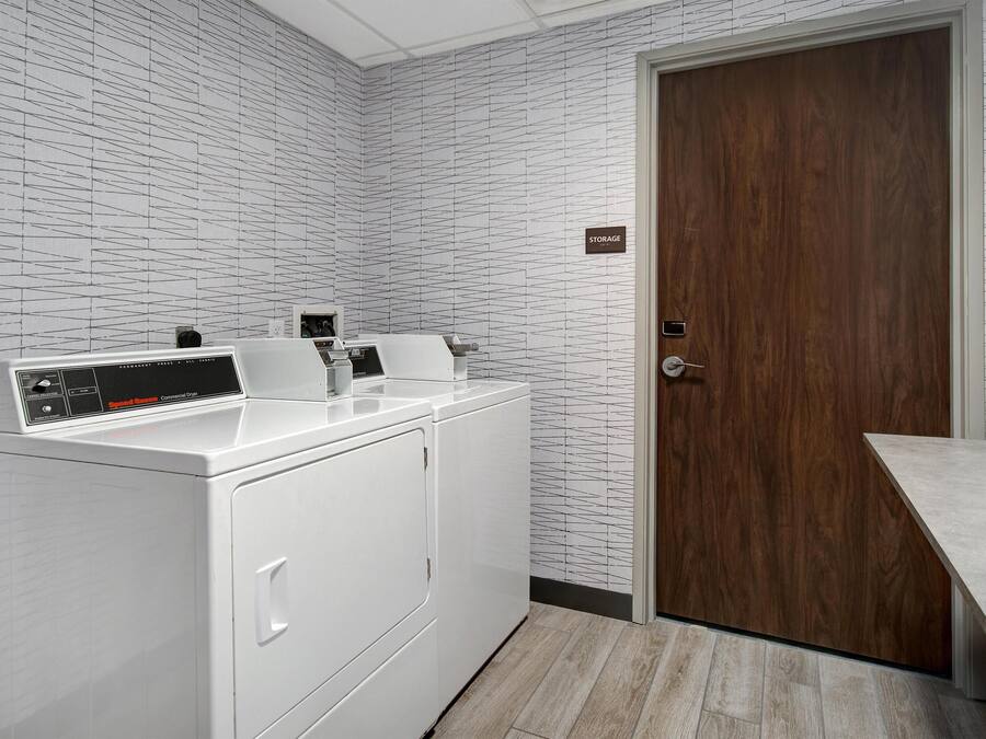 A laundry area with a white washing machine and dryer, a wooden door labeled "STORAGE", and a countertop.