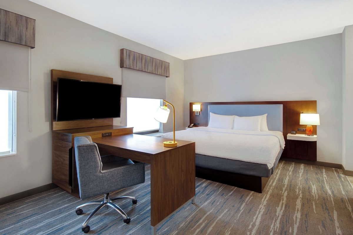 Habitación de hotel con cama, escritorio, silla, televisor y dos lámparas de noche.