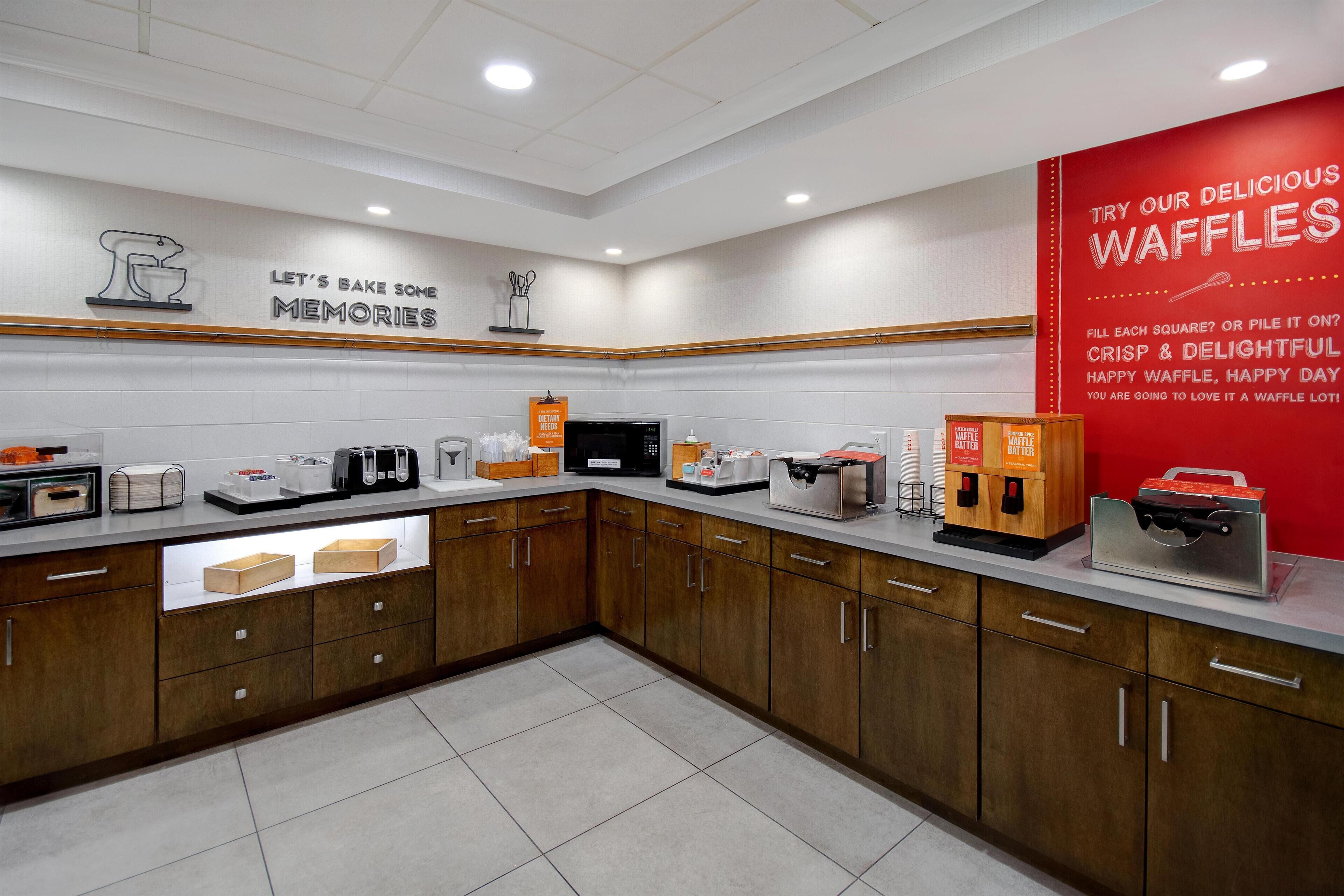 Un espacio tipo cocina con estación de gofres, incluyendo máquinas para hacer gofres y un cartel que promociona los gofres.
