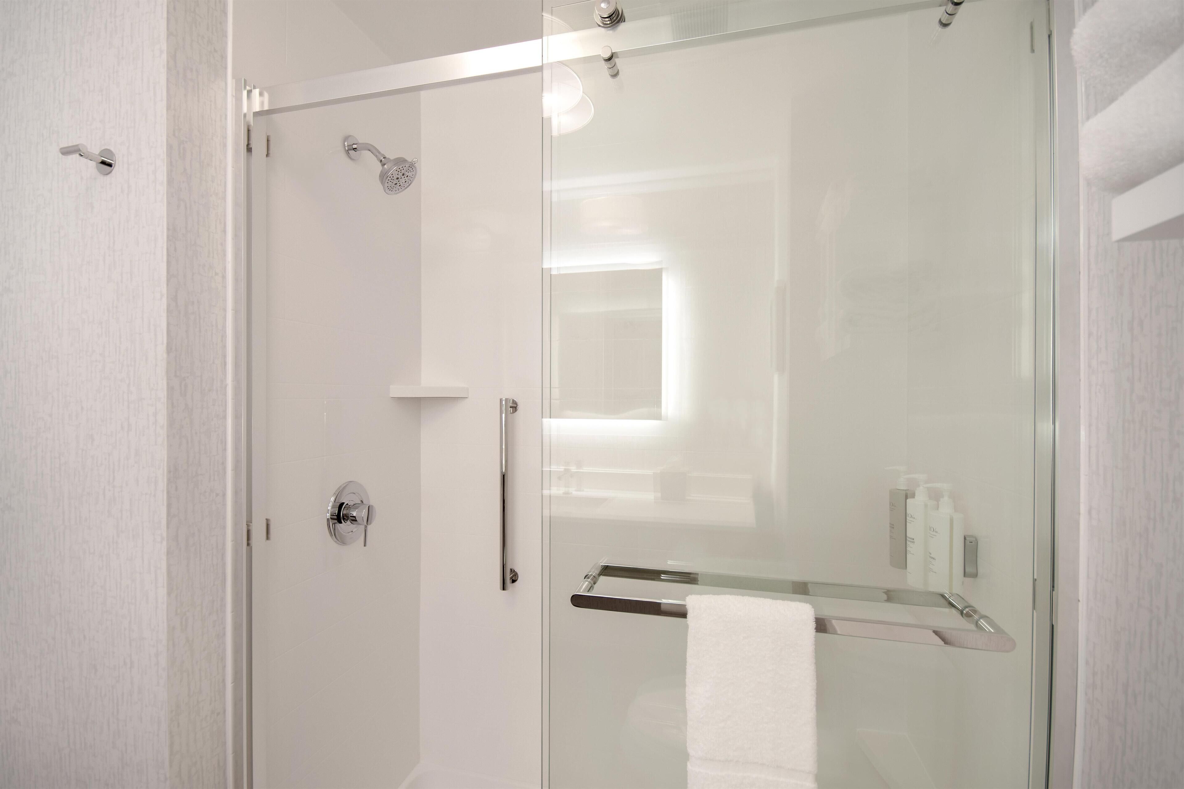 Ein modernes Badezimmer mit einer Duschkabine aus Glas, einem weißen Handtuchhalter und einer sichtbaren Shampoo-Flasche.