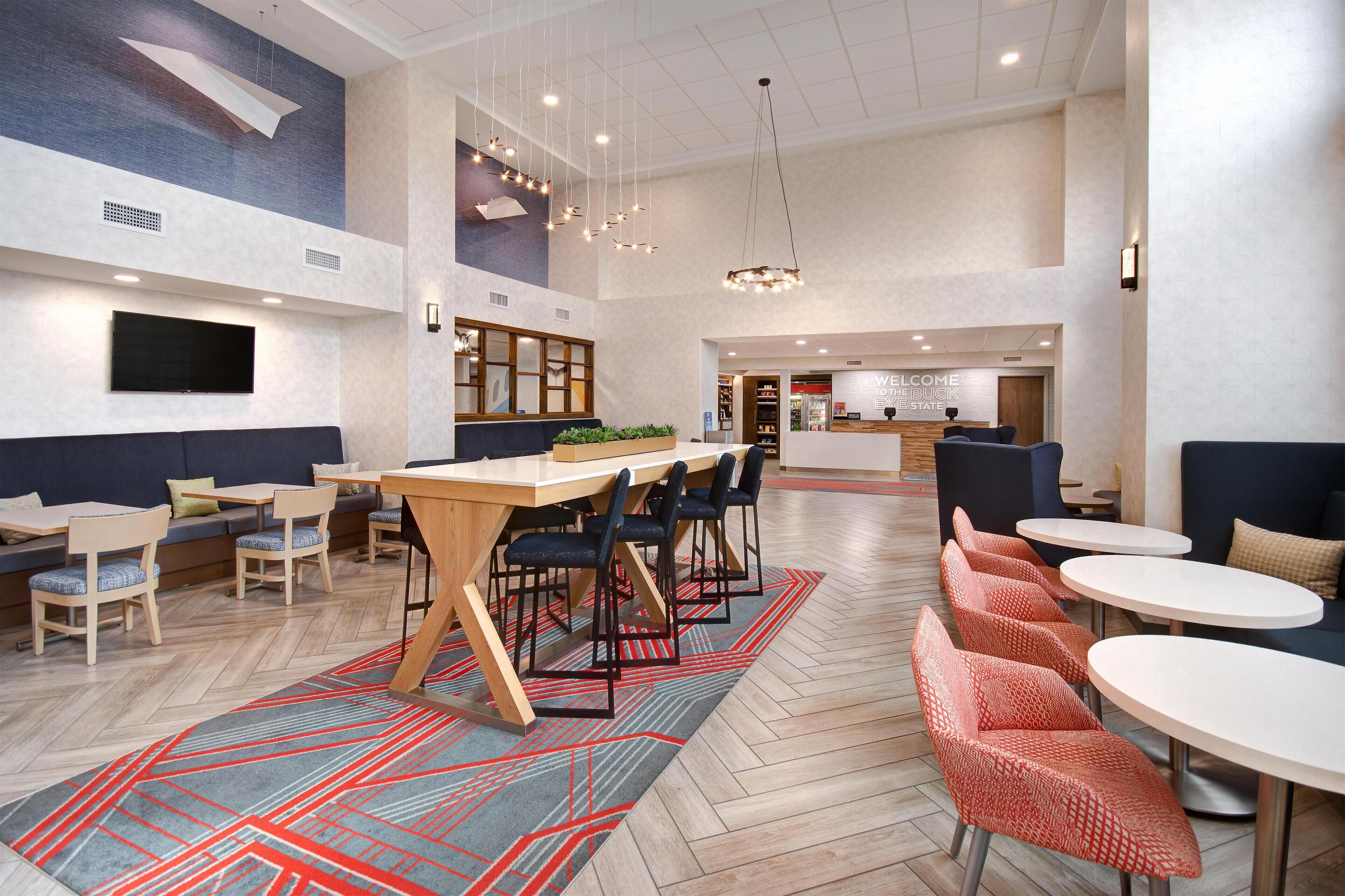 Un moderno hall de hotel con un amplio comedor, diferentes disposiciones de asientos y un mostrador de recepción.