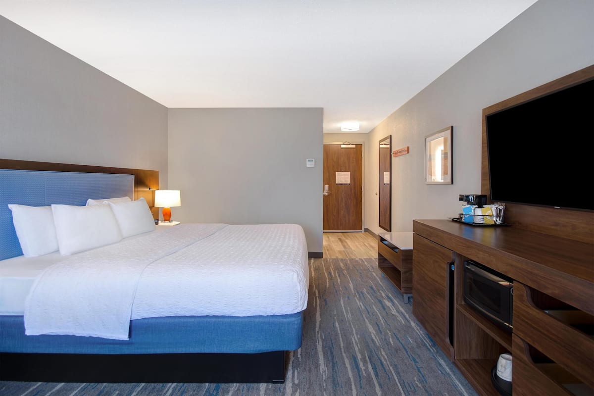 Habitación de hotel con una cama grande, un escritorio con televisor de pantalla plana, una lámpara y un aparador de madera.