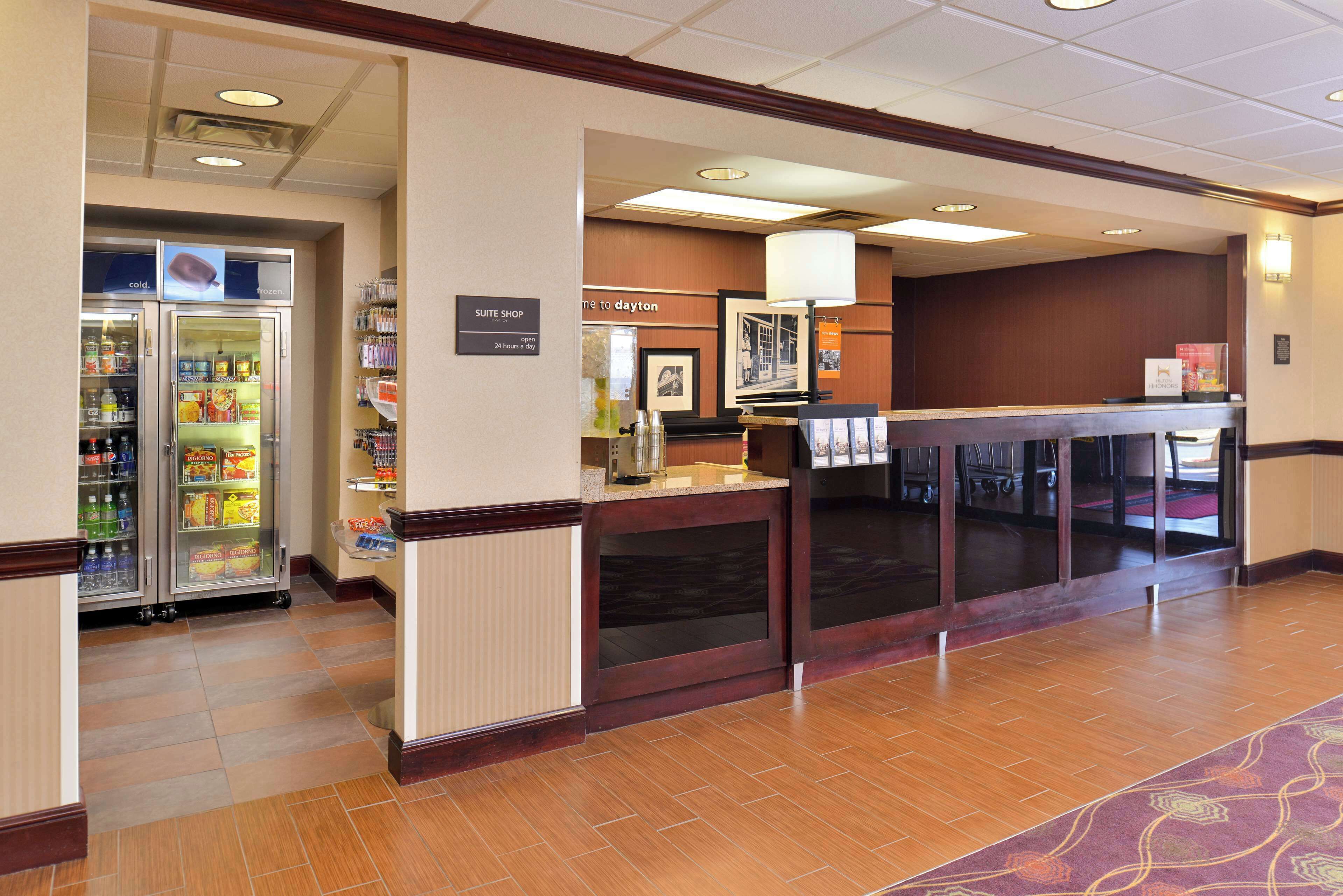 A hotel lobby with a reception desk, a suite shop, and a refrigerator stocked with beverages and snacks.