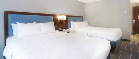 A hotel room with two beds, a nightstand, a lamp, and a door.