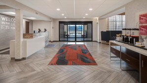 A modern reception area with a check-in counter, a patterned rug, and a view through the glass doors. - Hampton Inn & Suites Dayton - Vandalia (Dayton)