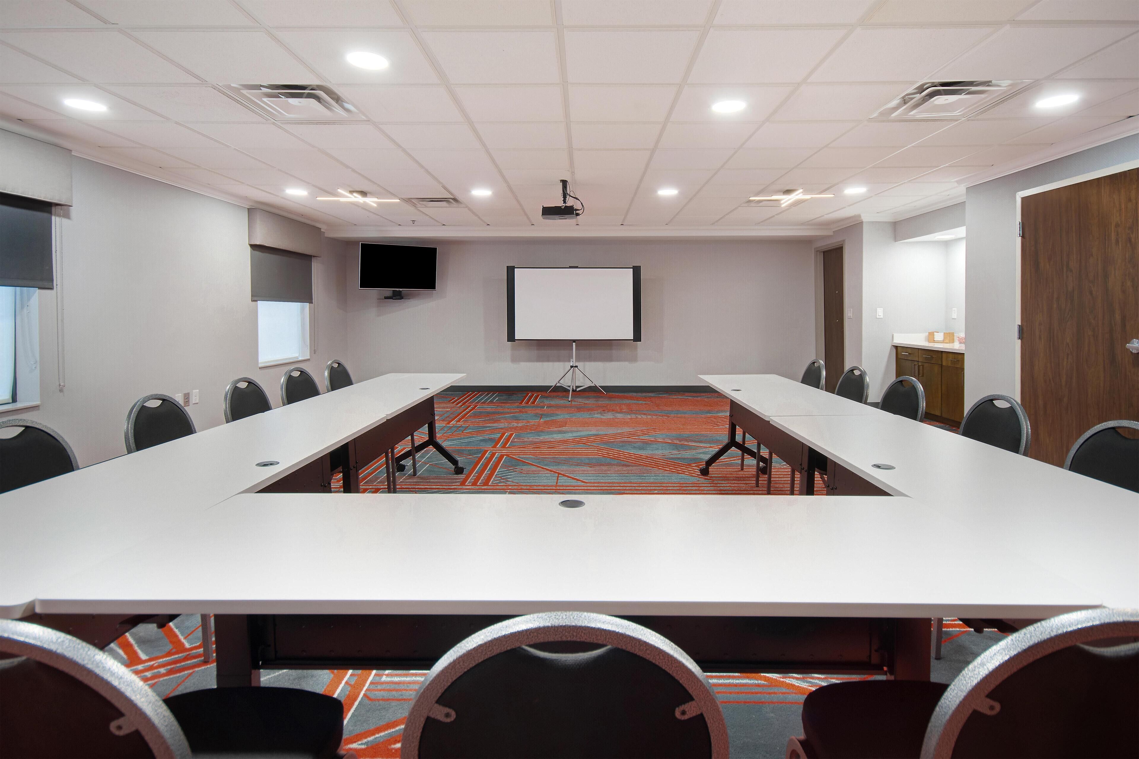 Une salle de conférence avec une longue table, des chaises, un écran de projection et un sol recouvert de moquette.