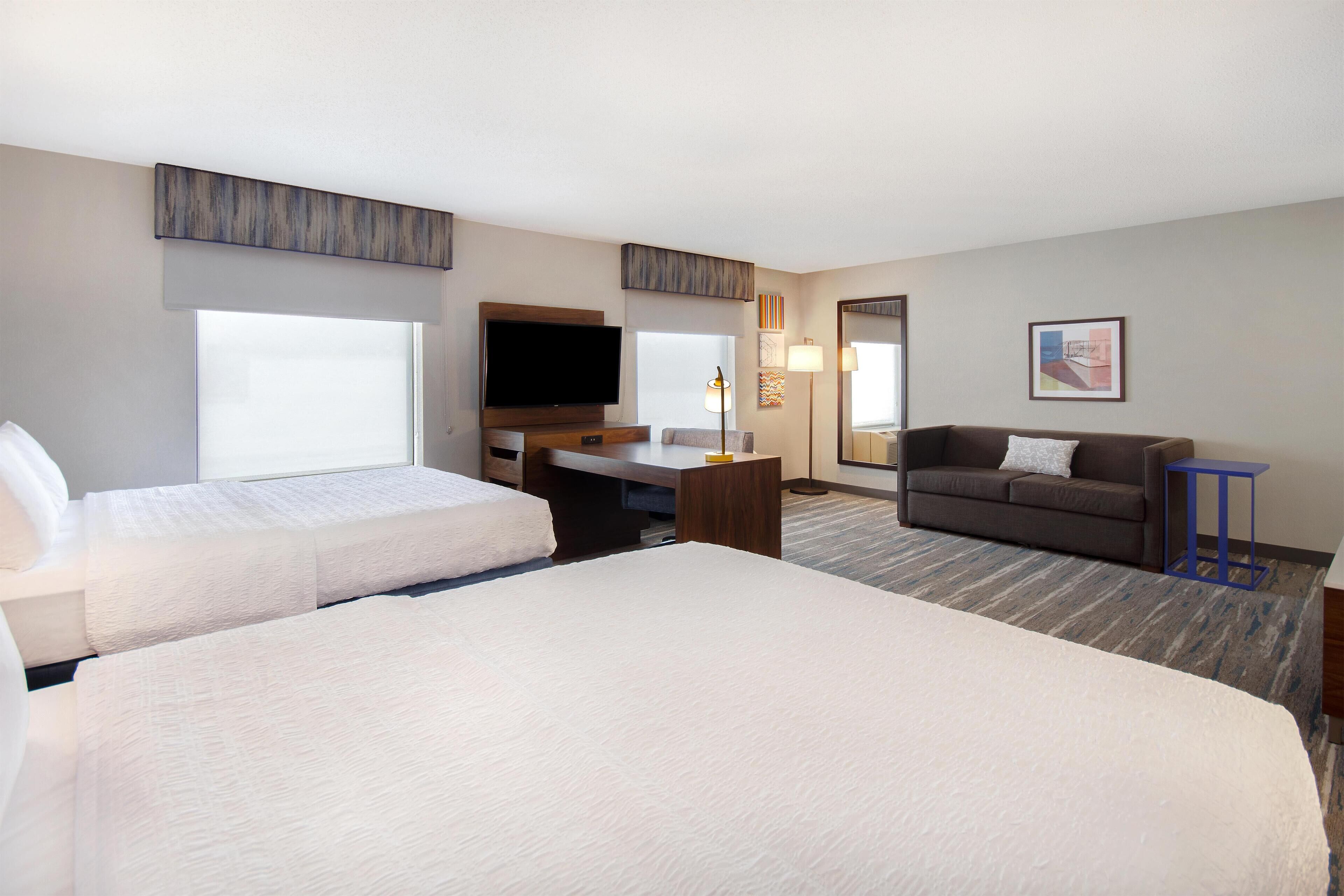 Een hotelkamer met twee bedden, een bureau, een bank, een televisie en een groot raam.
