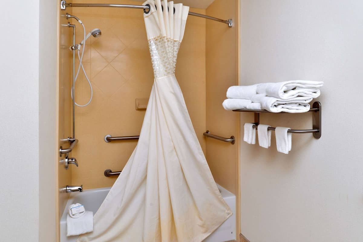 A bathroom with a shower, a towel rack with folded towels, and a shower curtain.