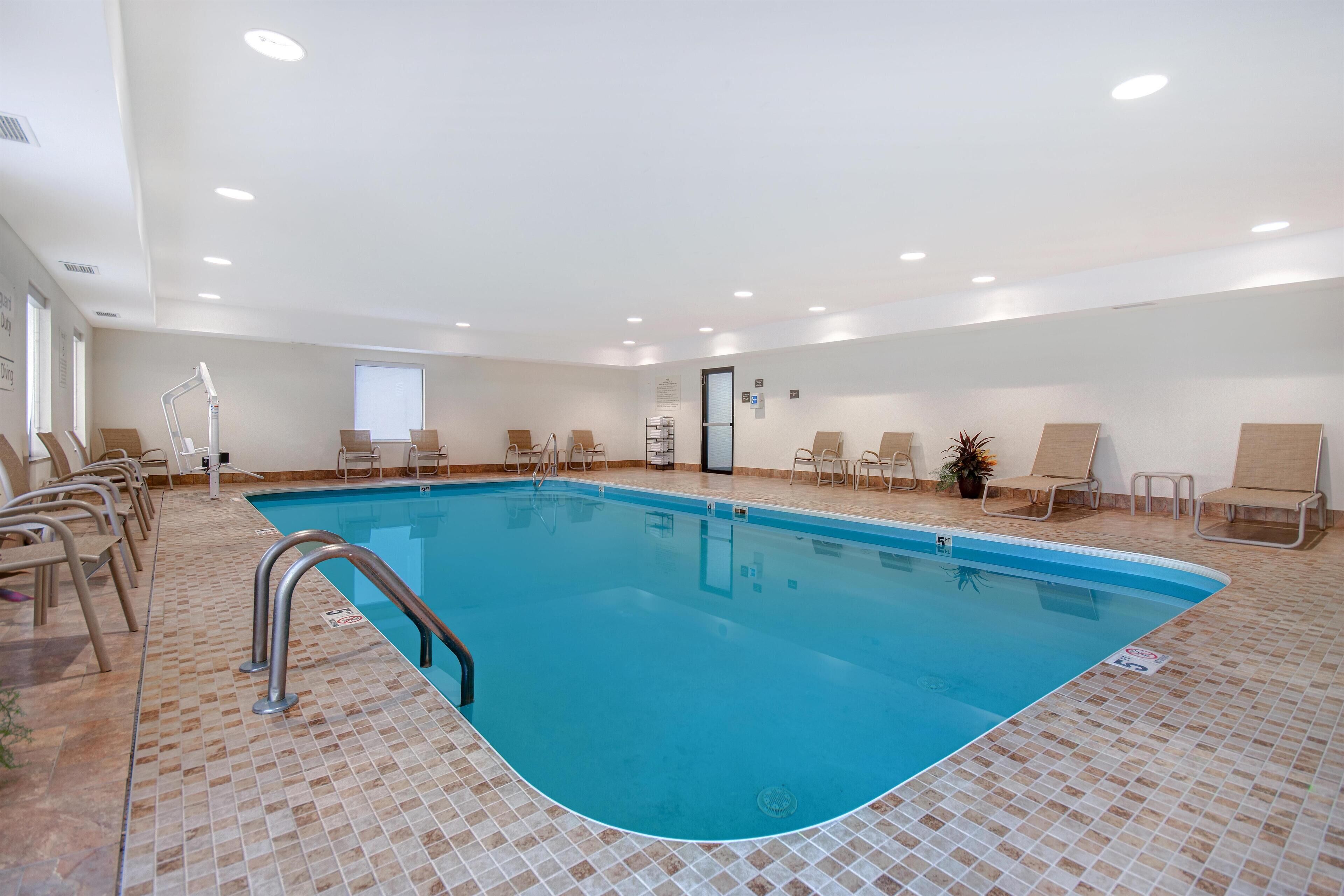 En inomhuspool med kakelbeklädd botten, en metallstege och flera solstolar runt poolområdet.