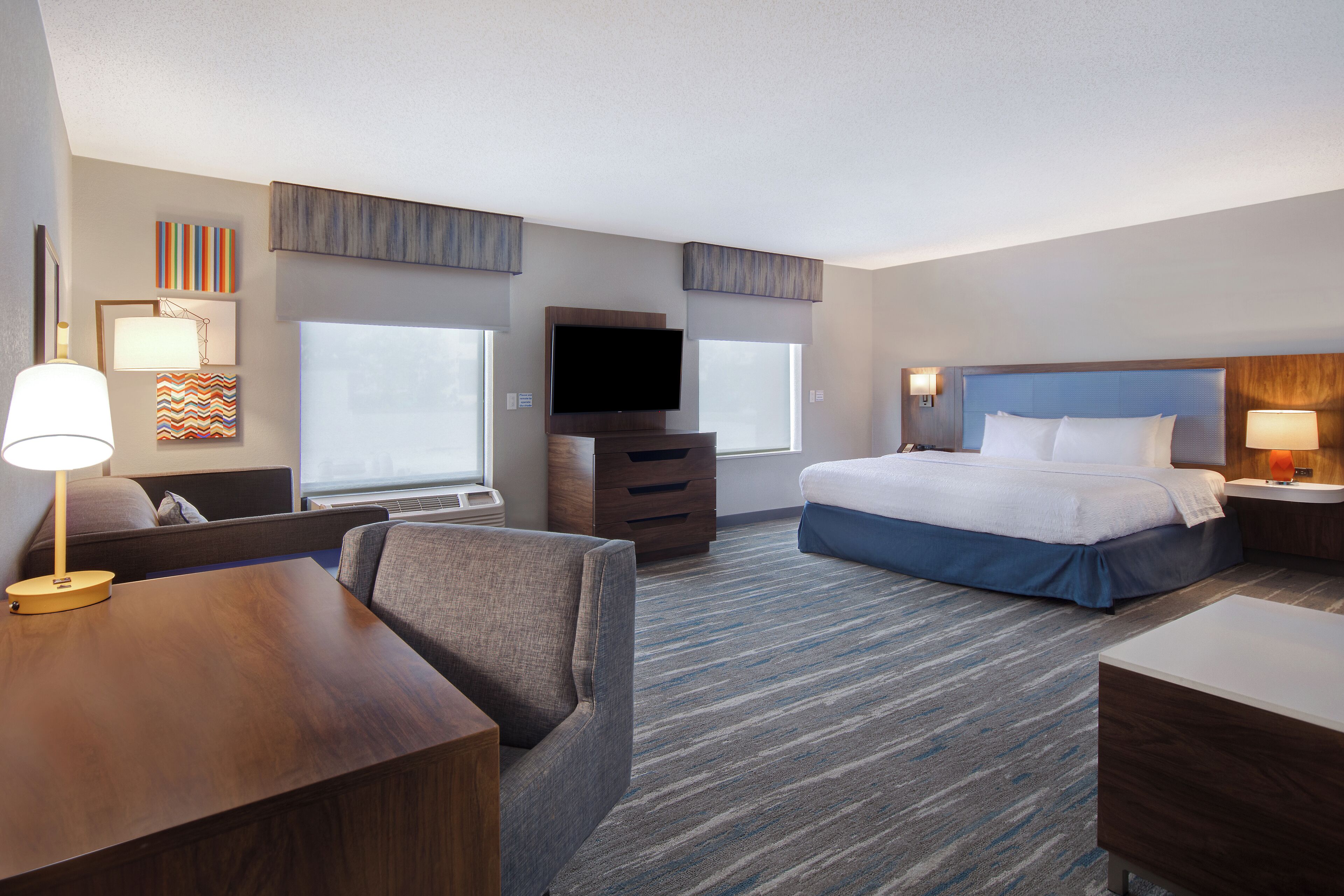 A hotel room with a bed, a desk, a chair, a TV, and a dresser.