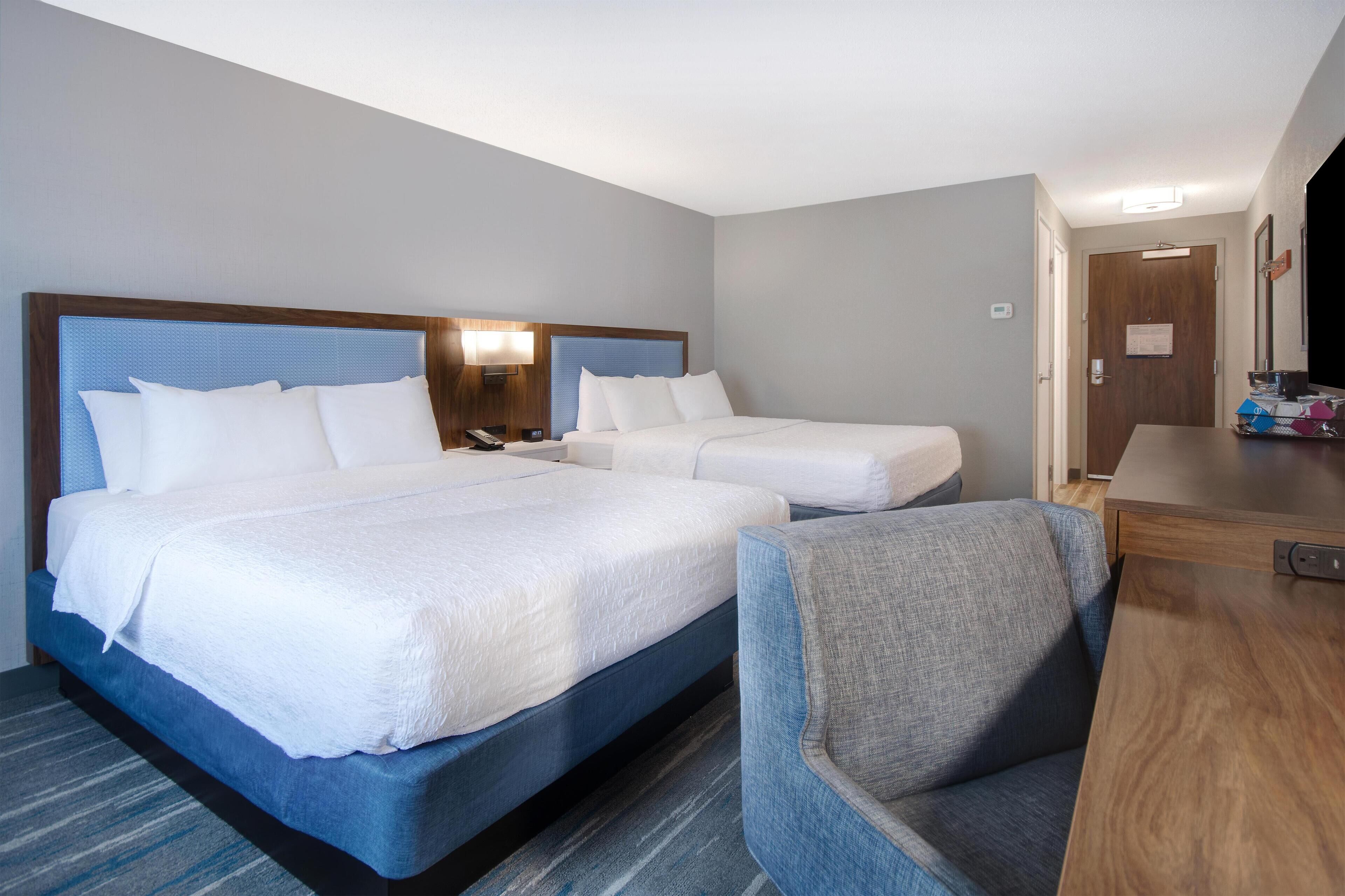 A hotel room with two beds, a desk, and a chair.
