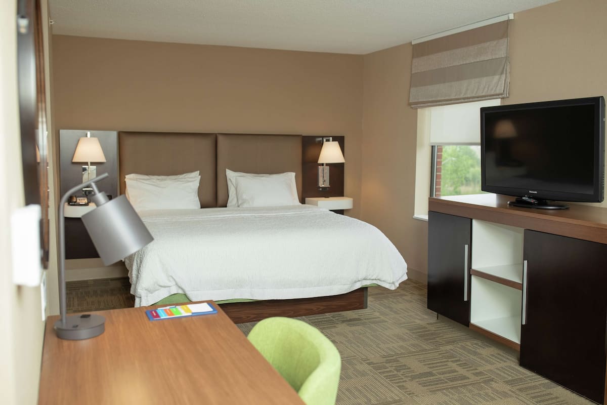 A hotel room with a bed, bedside lamps, a desk with a lamp, a television, and a window with blinds.