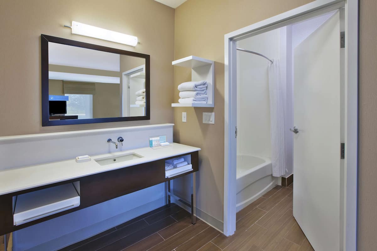 A modern bathroom with a white vanity, a large mirror, a shower, and a door leading to another room.