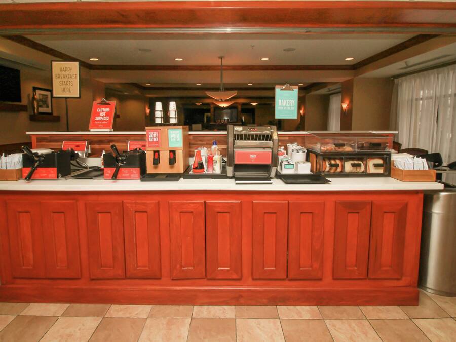 A breakfast bar with a coffee machine, a sign indicating breakfast starts here, and a caution sign about hot surfaces.