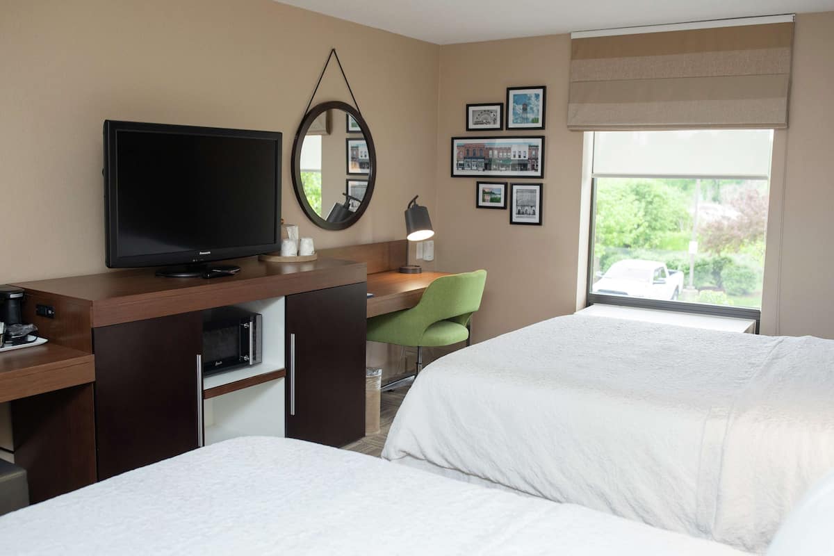 A hotel room with a bed, a desk with a television, a mirror, and framed pictures on the wall.