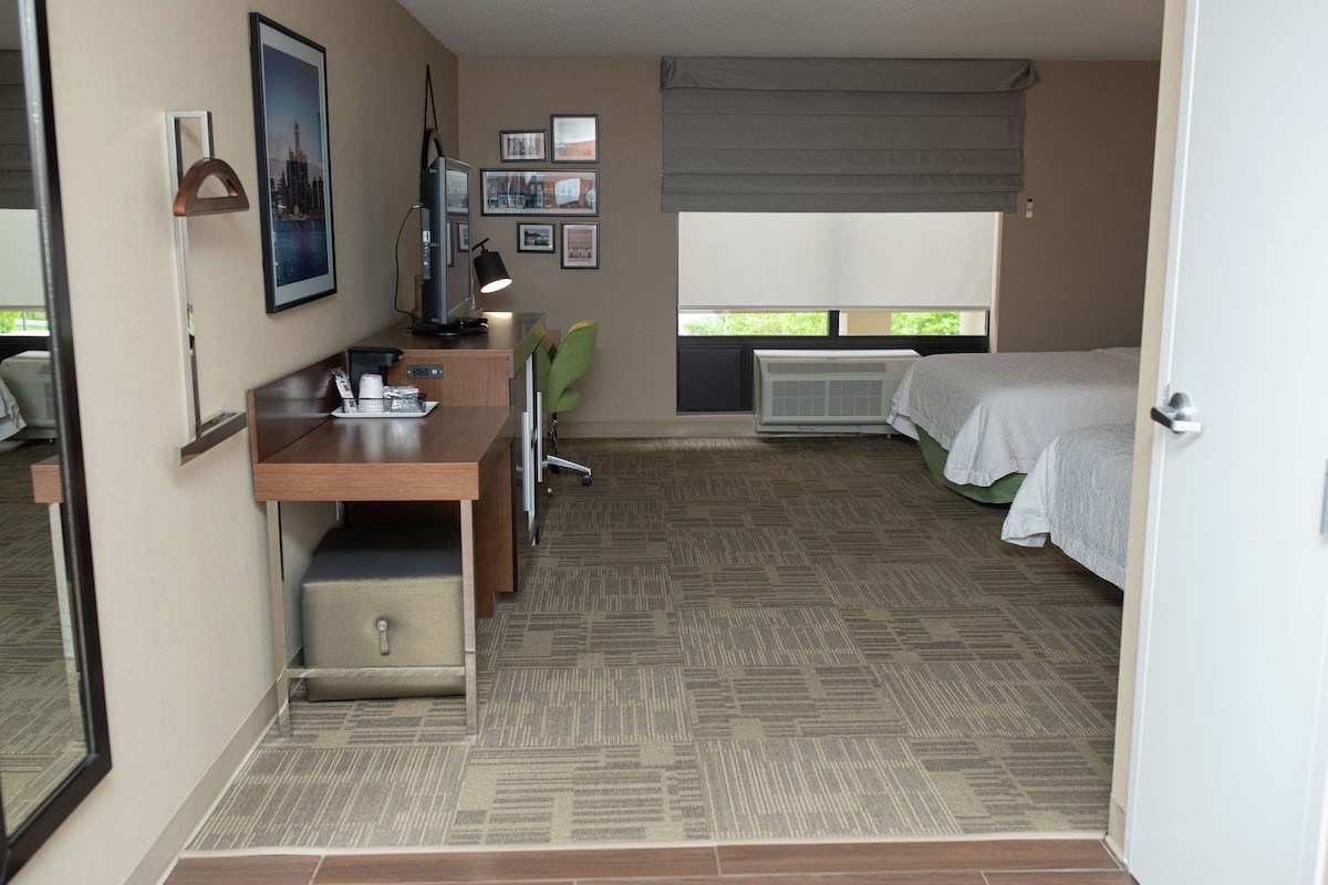 A hotel room with a bed, desk, chair, and a window with blinds.