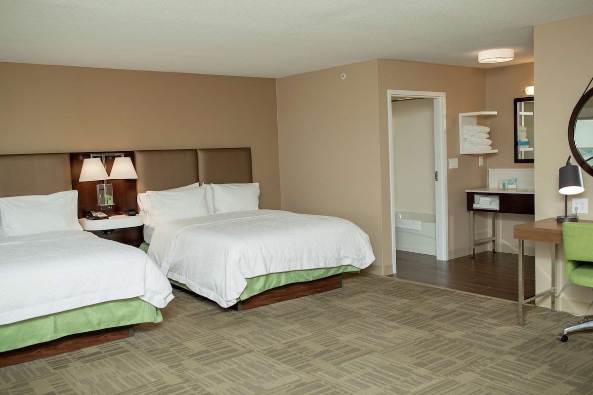 A hotel room with two beds, a desk, a chair, a mirror, and a bathroom door.
