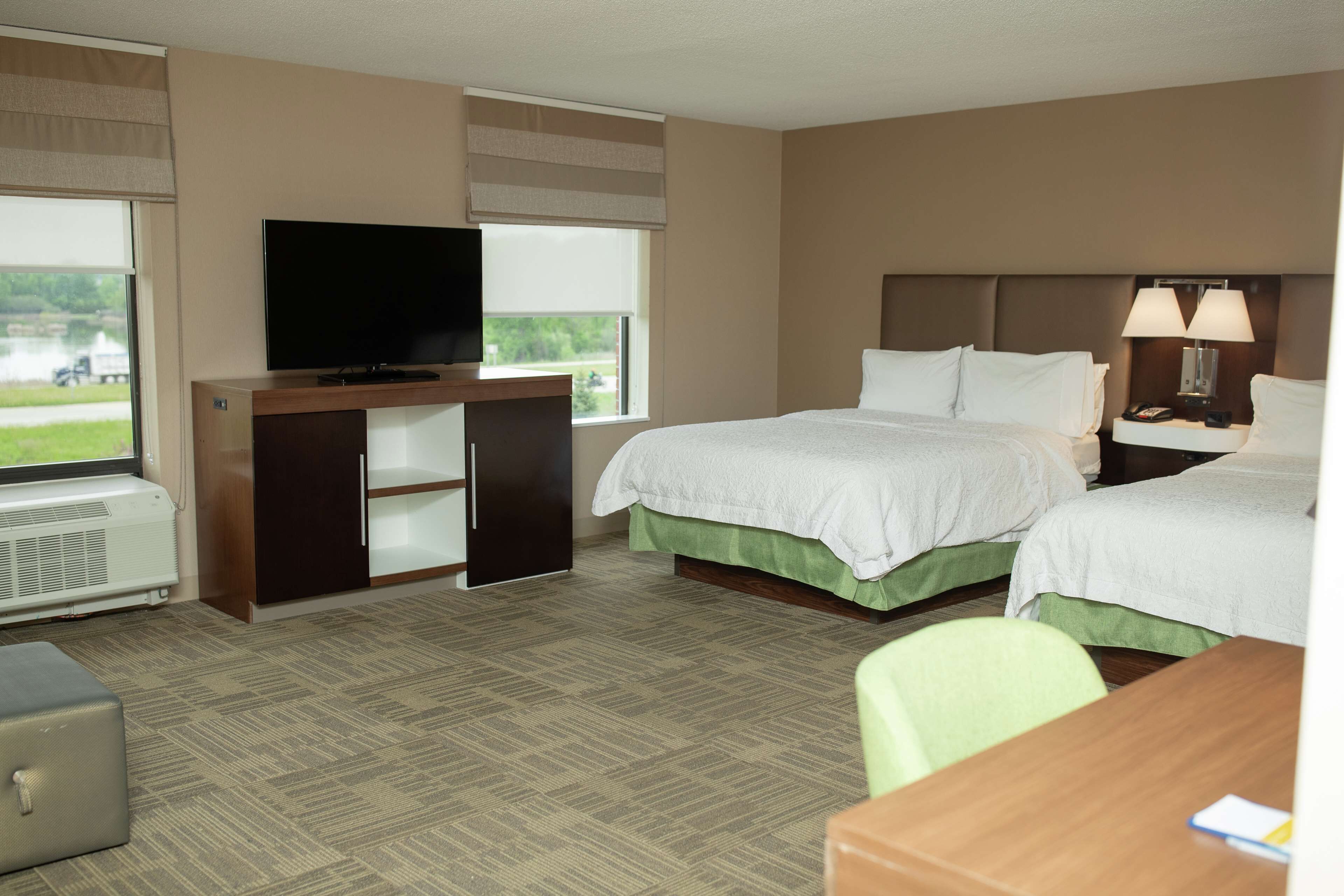 Quarto de hotel com duas camas, uma escrivaninha, televisão e janela com vista para um lago.