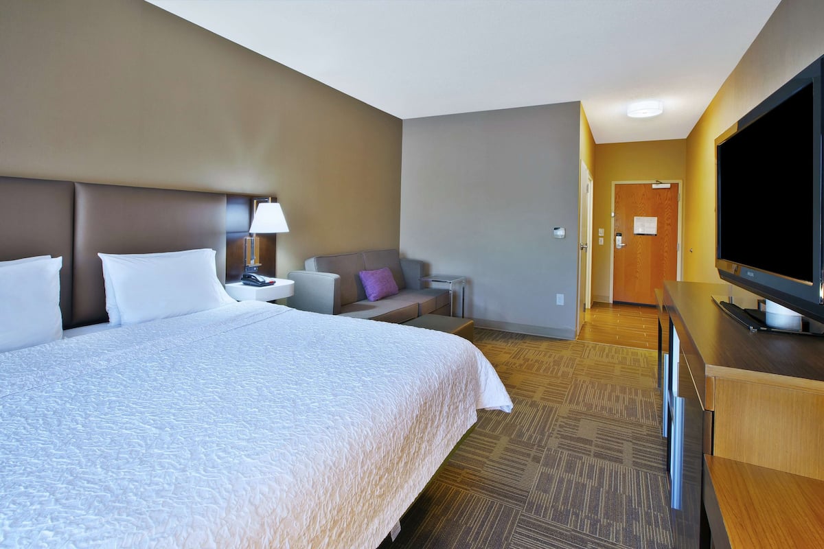 A hotel room with a large bed, a television, a desk, and a sofa.