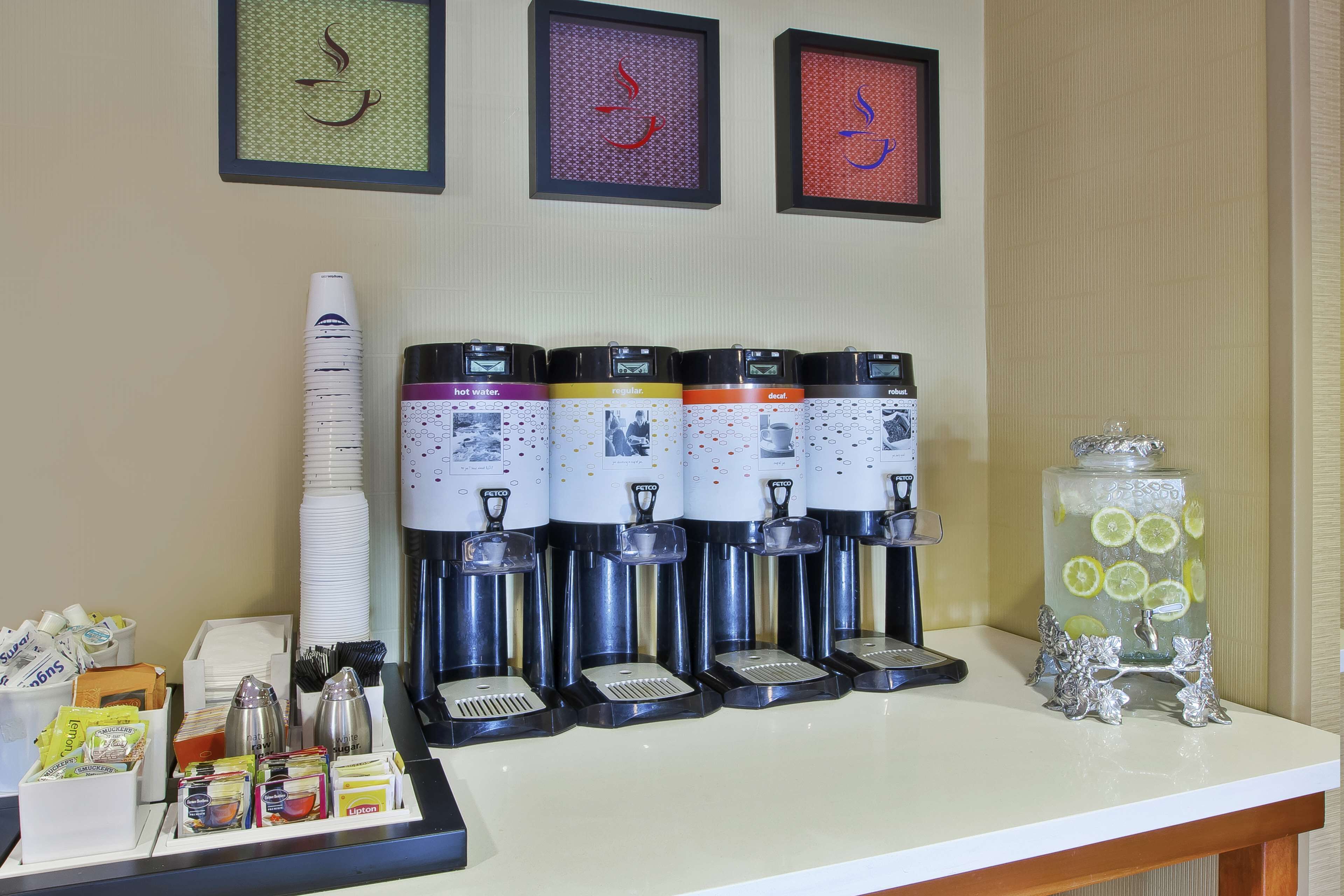 A coffee station with multiple dispensers, a glass jar with lemons, and various coffee pods and cups.