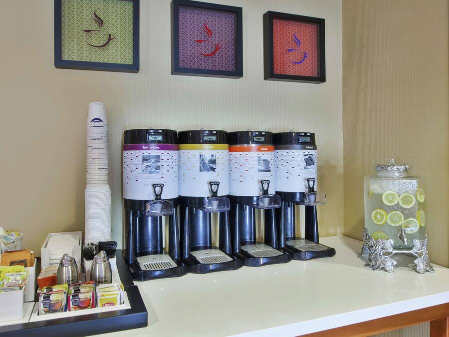 A coffee station with multiple dispensers, a glass jar with lemons, and various coffee pods and cups.