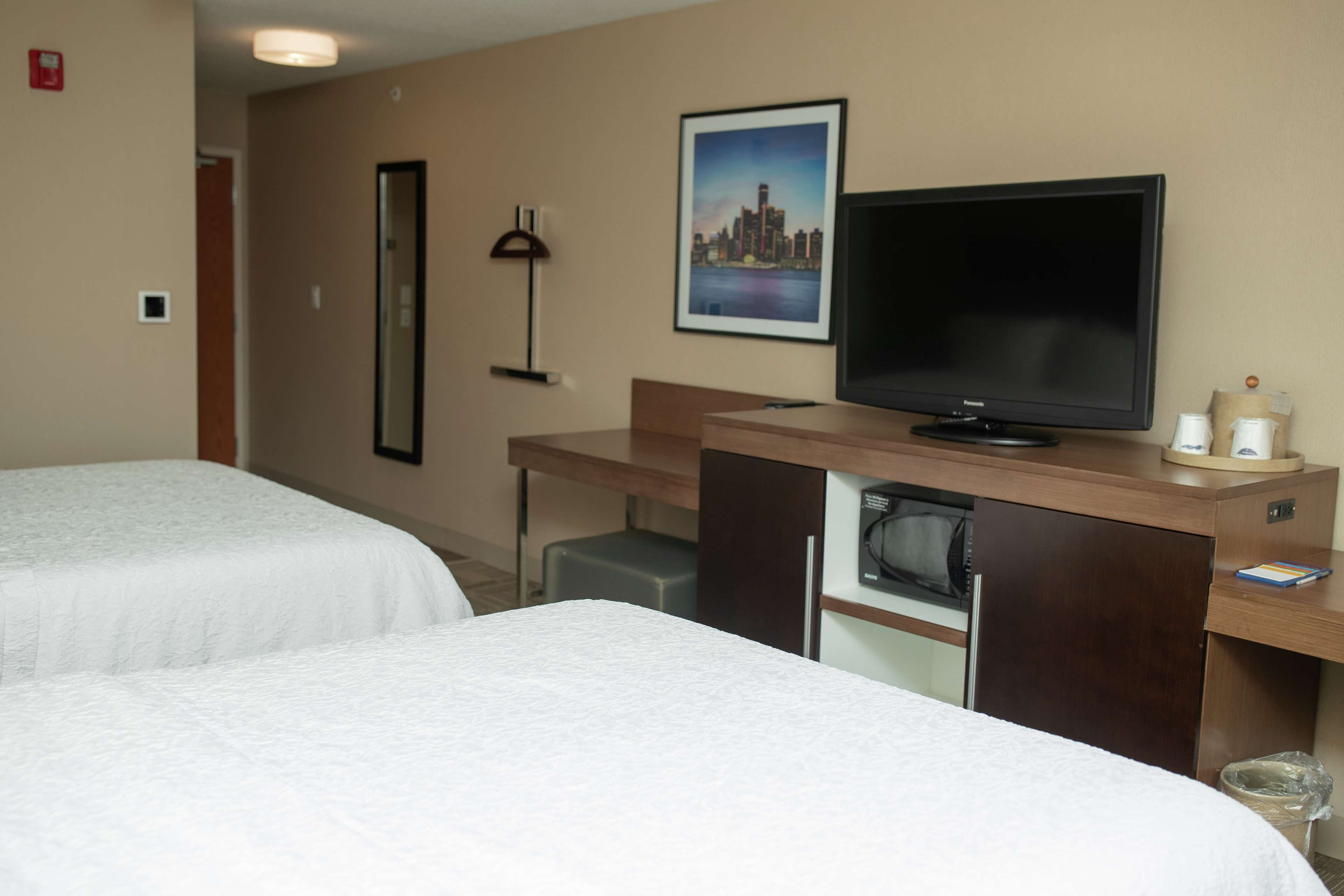A hotel room with two beds, a desk with a television, a mirror, and a framed picture on the wall.