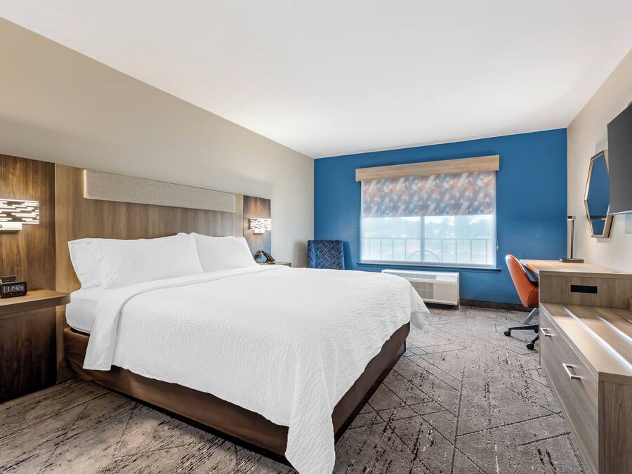 A modern hotel room with a large bed, a desk, a chair, and a television.