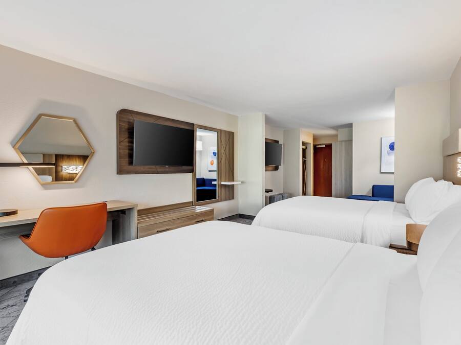A hotel room with two beds, a desk, a chair, a TV, and a mirror.