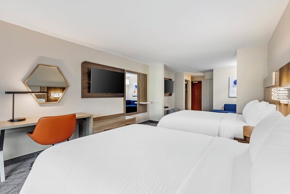 Quarto de hotel com duas camas, uma escrivaninha, uma cadeira, uma televisão e um espelho.